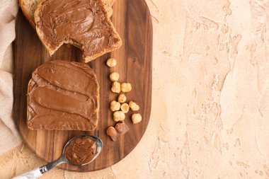 Wooden board of tasty toasts with hazelnut butter and nuts on color background