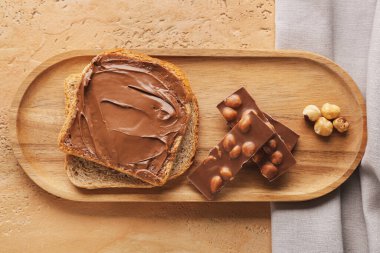 Wooden board of toasts with hazelnut butter and chocolate on color background