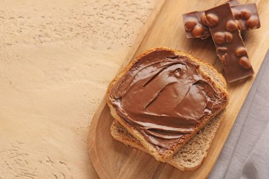 Wooden board of toasts with hazelnut butter and chocolate on color background, closeup