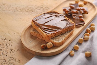 Wooden board of toasts with hazelnut butter and chocolate on color background, closeup