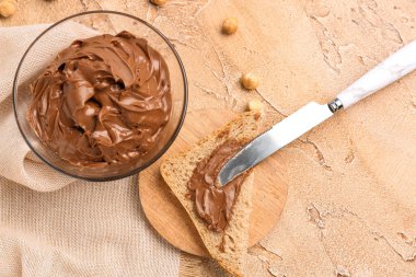 Bowl of tasty hazelnut butter and toast on color background