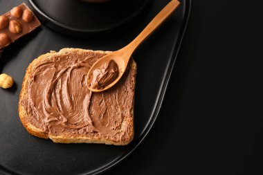 Board of tasty toast with hazelnut butter on dark background, closeup