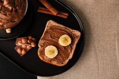 Board of tasty toast with hazelnut butter, banana, chocolate and cinnamon on table, closeup