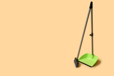 Green dustpan with broom on orange background