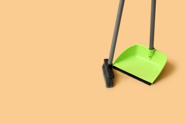 Green dustpan with broom on orange background