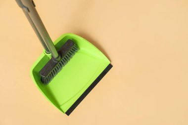 Green dustpan with broom on orange background