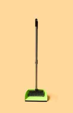 Green dustpan with broom on orange background