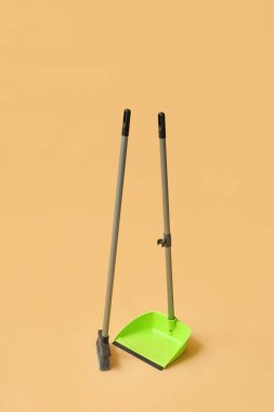 Green dustpan with broom on orange background