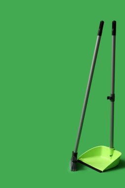 Dustpan with cleaning broom on green background