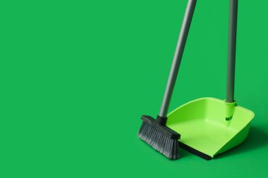 Dustpan with cleaning broom on green background