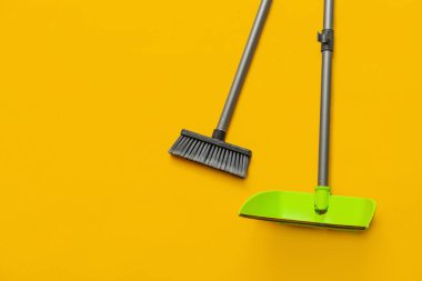 Cleaning broom with dustpan on yellow background
