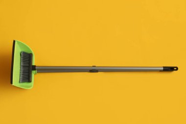 Cleaning broom with dustpan on yellow background