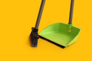 Cleaning broom with dustpan on yellow background