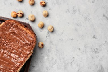 Tasty toast with hazelnut butter and nuts on light background