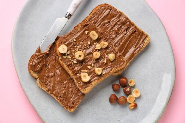 Plate of tasty toasts with hazelnut butter and nuts on pink background, closeup