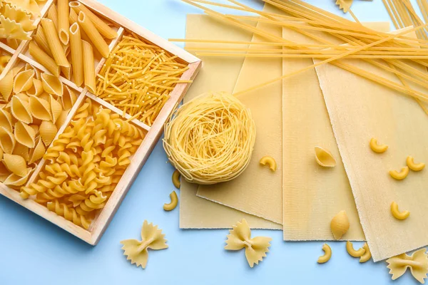 Box with different types of raw pasta on color background, closeup