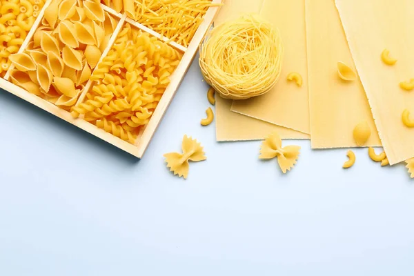 Box with different types of raw pasta on color background