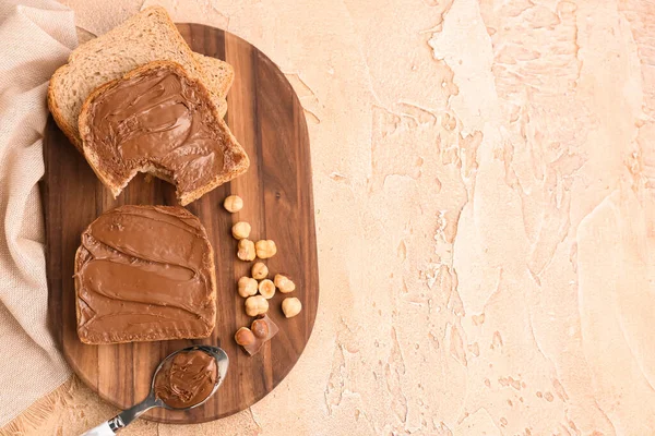 Wooden board of tasty toasts with hazelnut butter and nuts on color background