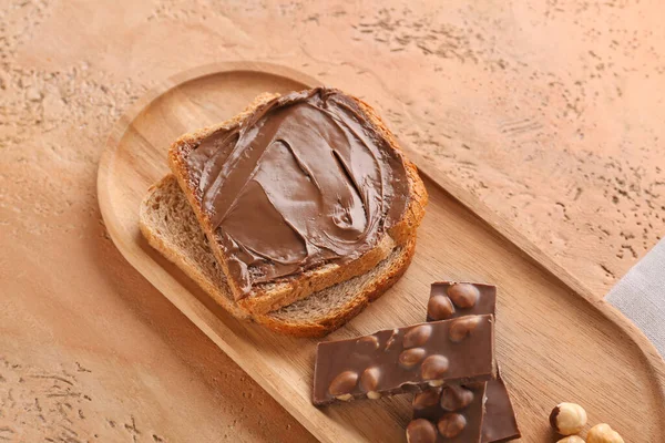 Wooden board of toasts with hazelnut butter and chocolate on color background