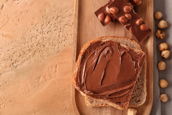 Wooden board of toasts with hazelnut butter and chocolate on color background, closeup