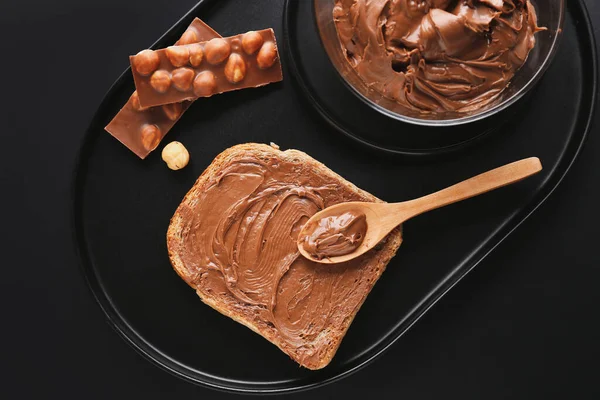 Board of tasty toast with hazelnut butter and chocolate on dark background, closeup