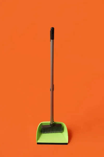 Plastic dustpan with cleaning broom on color background