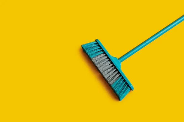 Blue cleaning broom on yellow background