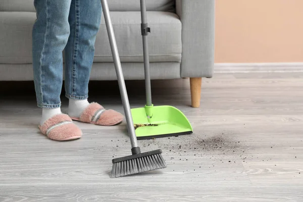 Woman sweeping rubbish with dustpan and broom at home