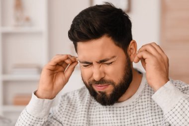 Young man with ear plugs suffering from loud noise at home, closeup