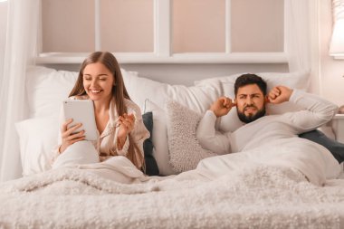 Young man cannot sleep because of his wife using tablet computer in bedroom