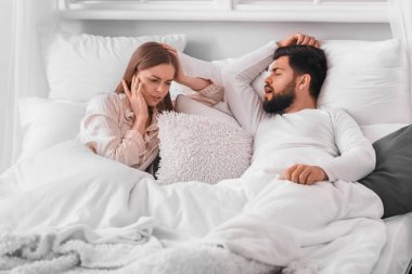 Young woman cannot sleep because of her snoring husband in bedroom