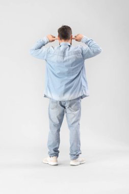 Young man suffering from loud noise on grey background, back view