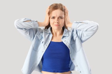 Young woman suffering from loud noise on grey background