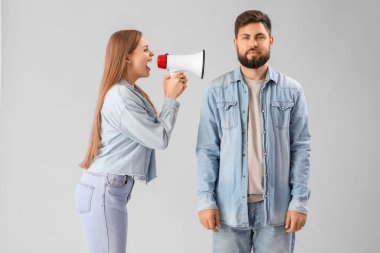 Young woman with megaphone shouting at her husband on grey background