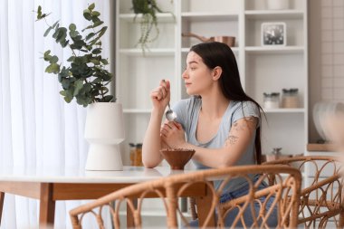 Young woman eating corn balls with spoon in kitchen