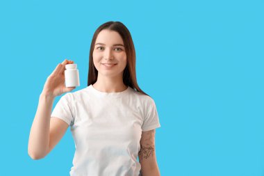 Young woman with bottle of vitamin supplements on blue background