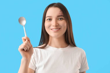 Young woman with silver spoon on blue background, closeup