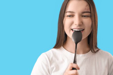 Young woman with silver spoon on blue background, closeup