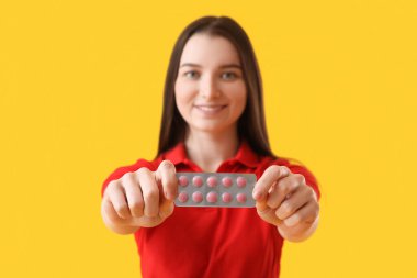 Young woman with blister of vitamin supplements on yellow background, closeup