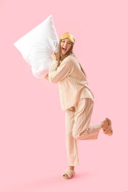 Young woman with sleeping mask and soft pillow on pink background
