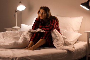 Upset young woman sitting on bed at night
