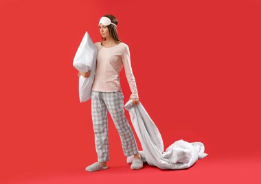 Beautiful woman with sleeping mask and blanket on red background