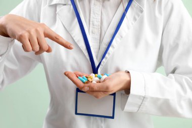 Female doctor pointing at pile of vitamin supplements on green background, closeup