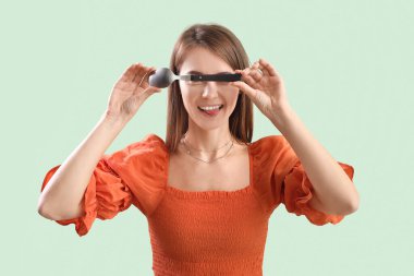 Beautiful woman with silver spoon on green background