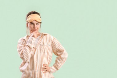 Thoughtful young woman in pajamas on green background