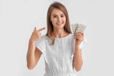 Beautiful woman pointing at blisters of vitamin supplements on grey background