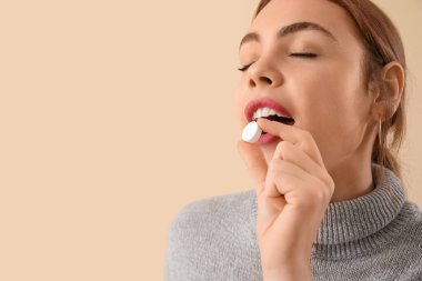 Beautiful young woman taking vitamin supplement on beige background, closeup