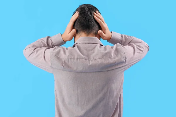 Young man suffering from loud noise on blue background, back view
