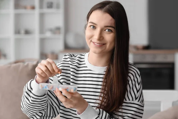 Young woman taking vitamin supplement from container at home