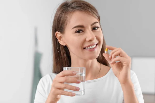 Beautiful woman with vitamin supplement and glass of water in kitchen, closeup